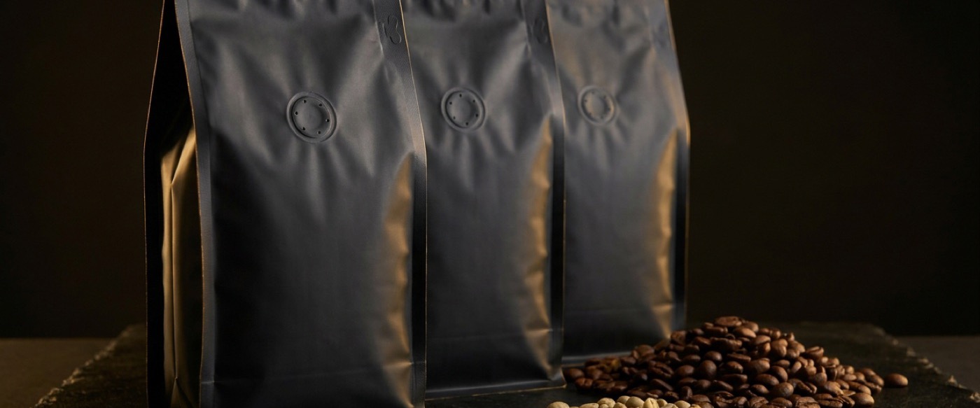 Three unbranded matte black coffee pouches beside roasted and green beans